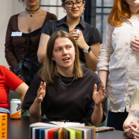 Kat Mellor sat at a table at a The Arena Speed Mentoring event, speaking as other attendees listen