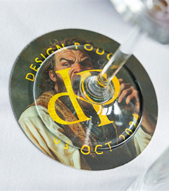 A drinks mat featuring the Design podge Logo on top of an oil painting style graphic of a man drinking from a bottle